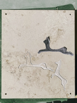 Close-up of the plaque during carving — two horses already chiseled out