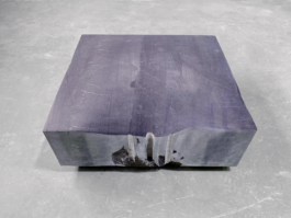 A large, flat gravestone made of dark Irish limestone in a workspace. The front edge has an irregular shape and deliberately preserved drill marks from where the stone was split.