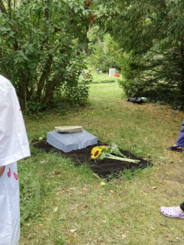 Eine Nahaufnahme des flachen Grabsteins aus irischem Kalkstein, der auf einem Rasengrab auf einem Friedhof aufgestellt ist. Eine kleinere, rohe Steinskulptur liegt auf dem Grabstein. Die Oberfläche des Steins ist leicht nach vorn geneigt.
