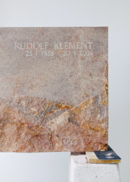 Detailansicht der Vorderseite des Grabsteins mit eingraviertem Namen und Daten über dem Gebirgsrelief