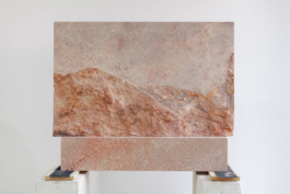 Atelieraufnahme eines Grabsteins aus Rochlitzer Porphyr mit rauem Relief, das eine Gebirgskette andeutet 