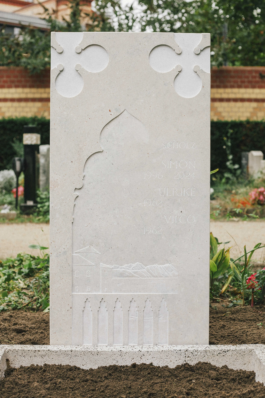 Finished gravestone in pink Untersberg marble standing in the cemetery, with a carved architectural relief on the front 