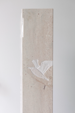 Side view of the marble gravestone showing a carved bird detail in low relief